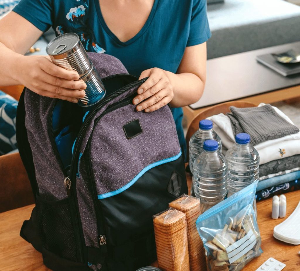 A person packs an emergency kit with water, food, first aid supplies, medications, a flashlight and other essential items.